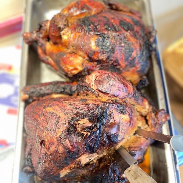 Two whole smoked chickens with crispy, dark skin in a metal pan, one being carved.