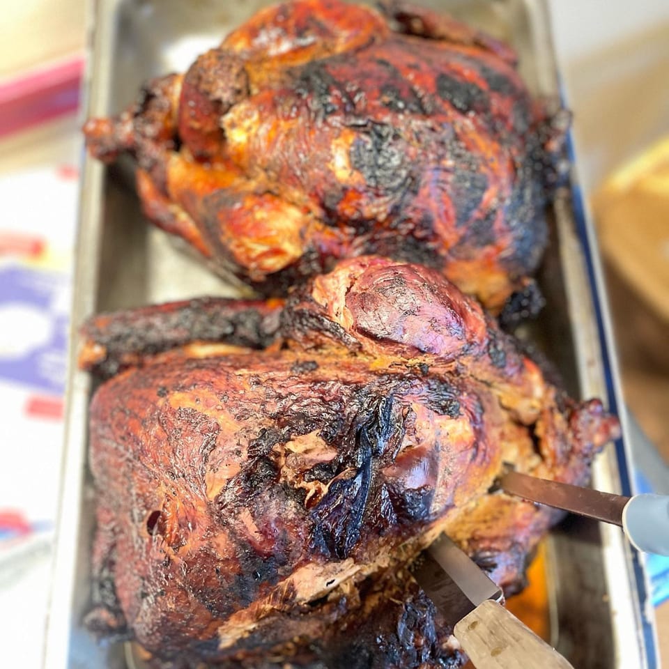 Two whole smoked chickens with crispy, dark skin in a metal pan, one being carved.