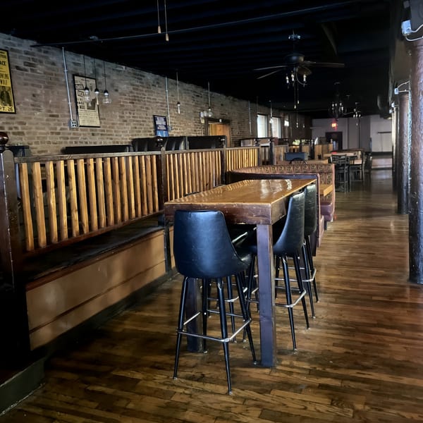 Interior of Five Ace's Smokestaq Lightning, featuring wooden tables, black chairs, and brick walls.